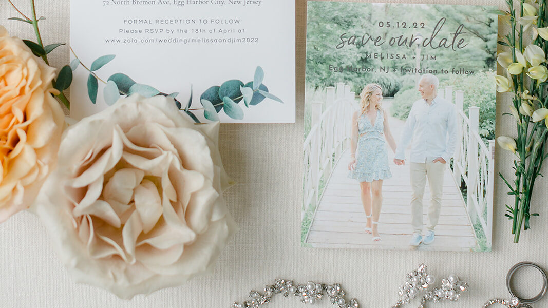 Flat lay of bridal details including "save the date" card, invitation and loose blooms by Leigh Florist. 