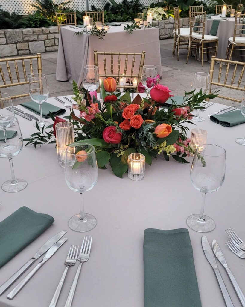 compact low lush wedding centerpiece with brightly colored roses and tulips and featuring votive candles set to maximize space on a small table