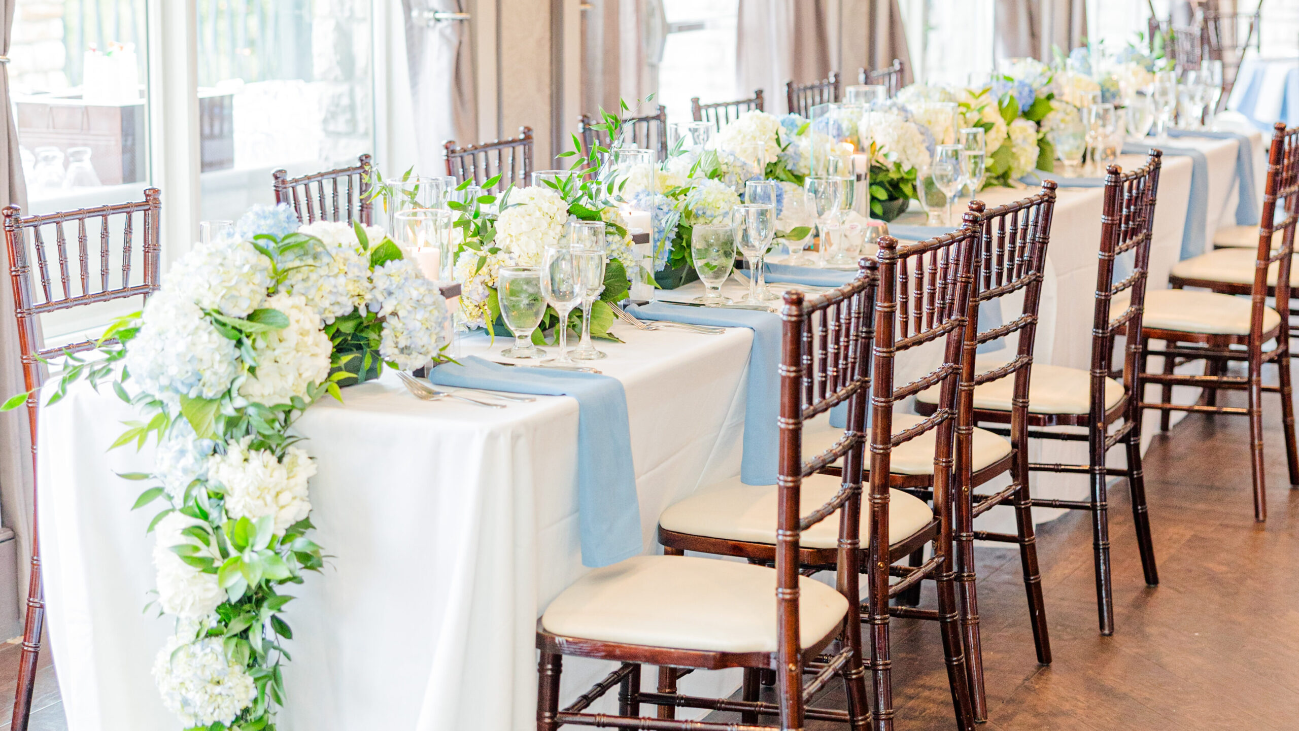 long wedding banquet table with blue napkins and coordinating low lush hydrangea centerpiece with garden greens