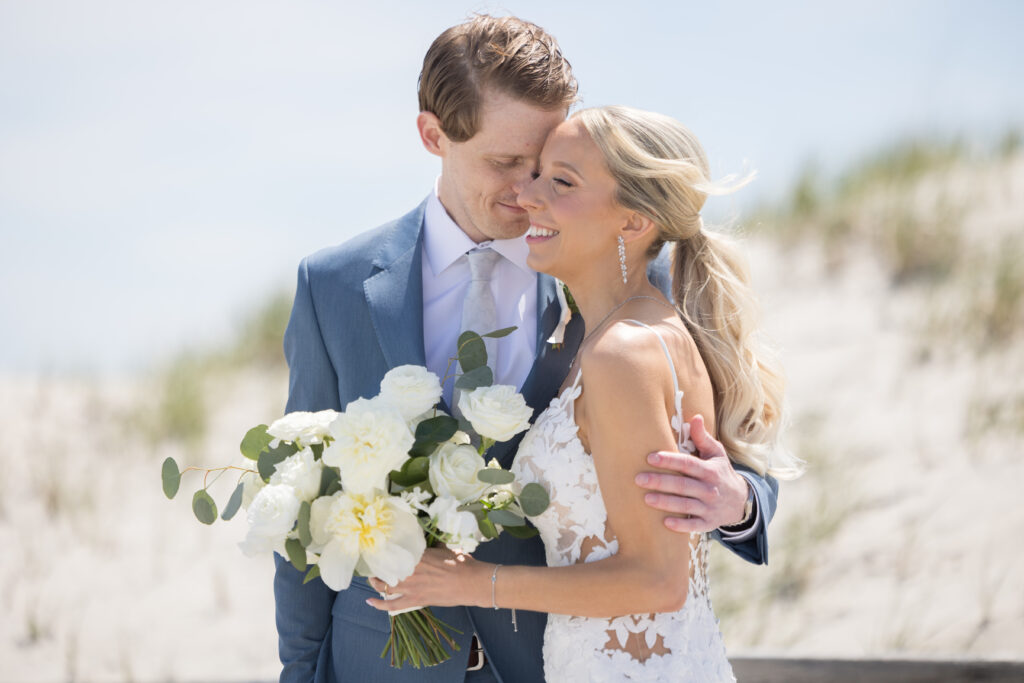 Bride and Groom on wedding day at ICONA Windrift. Bride is holding a bouquet of  white roses, ranunculus, and greenery.